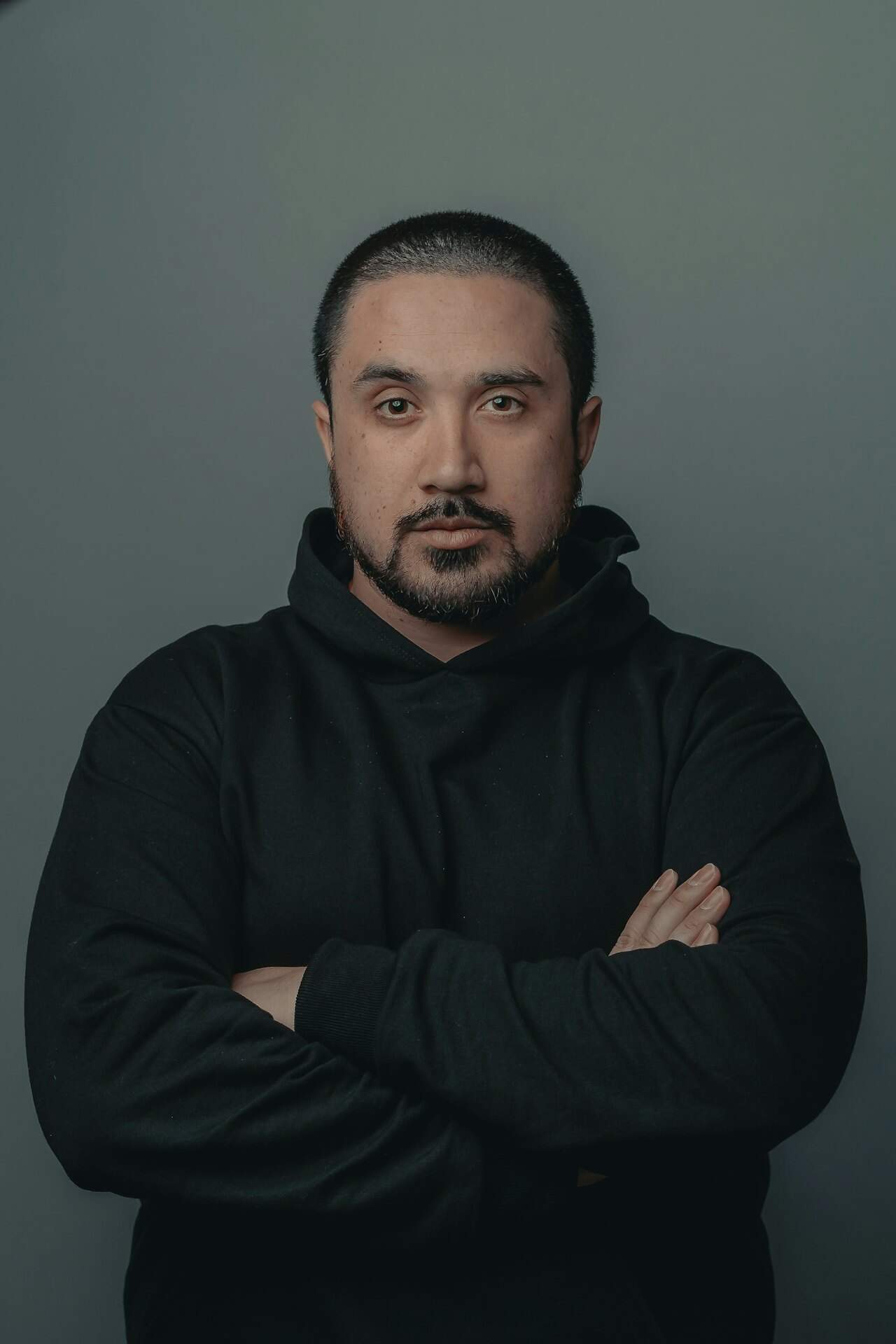 Professional man with crossed arms in black hoodie, neutral background.